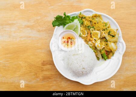 Gebratener Tintenfisch in Currypulver mit Reis und Fischsauce gemischt Chili in weißer Schüssel auf Holztisch rühren. Stockfoto