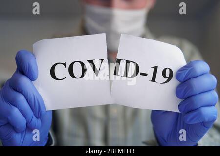 Herrenhände in blauen Handschuhen zerreißend Papier mit der Aufschrift covid-19. Sieg über das Corona-Virus. Konzept der Beendigung der Pandemie covid 19 Stockfoto