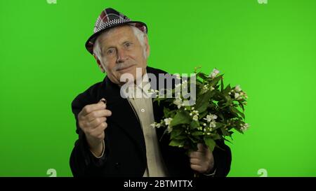 Ältere stilvolle Großvater kaukasischen reifen Mann mit Blumenstrauß und einem Verlobungsring auf Chroma-Schlüssel Hintergrund. Alte ältere Großeltern in Mode Kleidung geht auf Datum mit Frau. Grüner Bildschirm Stockfoto