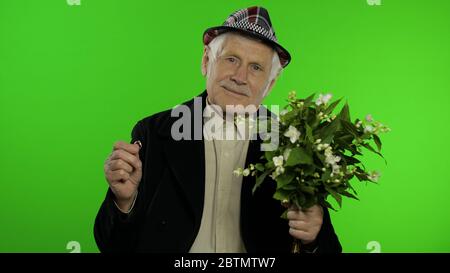 Ältere stilvolle Großvater kaukasischen reifen Mann mit Blumenstrauß und einem Verlobungsring auf Chroma-Schlüssel Hintergrund. Alte ältere Großeltern in Mode Kleidung geht auf Datum mit Frau. Grüner Bildschirm Stockfoto