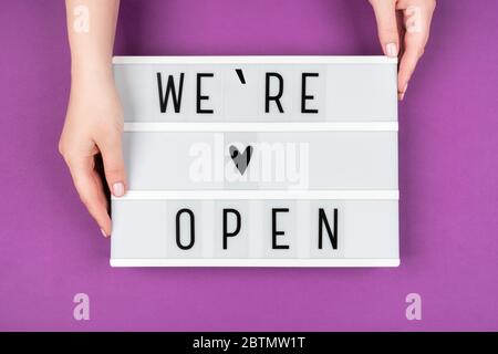 Wir sind offener Text auf einem Leuchtkasten auf einem violetten Hintergrund in den Händen von Frauen. Stockfoto