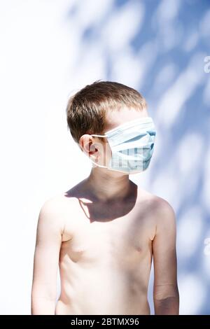 Ein 5-jähriger Junge, der eine PSA-Gesichtsmaske vor weißem Hintergrund trägt. Stockfoto