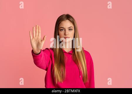 Geste anhalten. Strenge Teenager-Mädchen in rosa Hoodie hebt die Hand Stockfoto