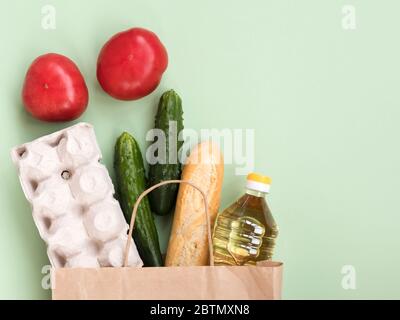 Essen in einem Papierbeutel: Eier, Gurke, Öl, Tomaten und Baguette auf grünem Hintergrund Stockfoto