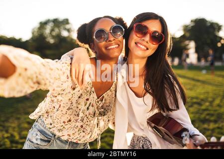 Zwei schöne Mädchen in Sonnenbrille freundlich umarmen einander, während glücklich, Fotos zusammen in Stadtpark Stockfoto