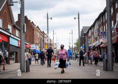 Eine Frau mit Gesichtsmaske geht nach der Einführung von Maßnahmen, um das Land aus der Blockaden zu bringen, in Walthamstow, East London, entlang einer Hauptstraße. Stockfoto