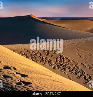 Die herrlichen Dünen von Maspalomas auf Gran Canaria, bei Sonnenuntergang mit einer einsamen Person im Hintergrund, die auf das Meer starrt Stockfoto