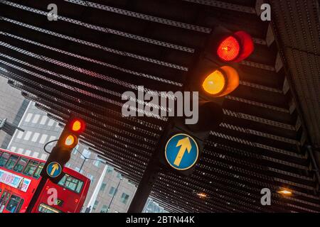 Die Ampel leuchtet rot und bernsteinfarben unter einer Eisenbahnbrücke, im Hintergrund fährt ein roter Londoner Bus an der London Bridge Station vorbei Stockfoto