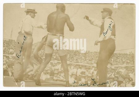 Fotopostkarte von James J. Jeffries, der von Jack Johnson wegschwingend ist. Eine schwarz-weiße Fotopostkarte des 'Kampfes des Jahrhunderts' zwischen Jack Johnson und James J. Jeffries. Auf dem Foto sieht man Jeffries im Hintergrund, der von Johnson wegschwingend ist. Zwei Beamte stehen auch im Ring. Stockfoto