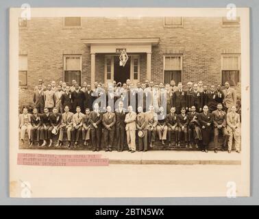 Foto von Kappa Alpha PSI Mitgliedern. Dieses Schwarz-Weiß-Foto zeigt Mitglieder der Kappa Alpha PSI Bruderschaft vor dem Haus des Alpha Kapitels während des Regionaltreffens der Nordzentralprovinz. Die erste Reihe ist in drei Reihen angeordnet und befindet sich vor dem Gebäude vor allem an einer niedrigen Ziegelwand. Stockfoto