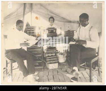 Foto von BC Franklin IH Spears und Effie Thompson. Ein Schwarz-Weiß-Foto von B.C. Franklin (rechts) und I. H. Spears (links), mit Secretary Effie Thompson (Mitte), in ihrem temporären Zeltbüro nach dem Tulsa Race Riot, 1921. Franklin und Spears sitzen auf beiden Enden eines Schreibtisches, der die Kamera zeigt. Stockfoto