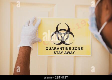 Frontline-Arbeiter, die Banner von Covid-19 oder Coronavirus Quarantäne Zone anbringen, bleiben weg vor der Tür im Krankenhaus als Vorsichtshinweis. Stockfoto