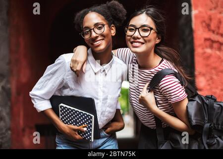 Zwei hübsche lächelnde Mädchen in Brillen mit Laptop und Rucksack glücklich in der Kamera suchen Stockfoto