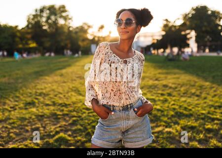 Junge schöne afrikanische Frau in Sonnenbrille verträumt in der Kamera suchen, während Sie Zeit in Stadtpark Stockfoto