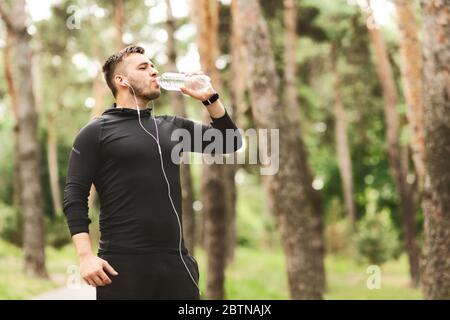 Sportler, der Mineralwasser trinkt, im Wald steht Stockfoto