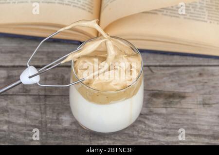 Dalgona Kaffee und offenes Buch auf rustikalem Holzhintergrund. Draufsicht. Stockfoto