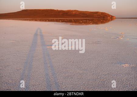 Rosa Salzsee bei Sonnenuntergang. Schatten Silhouette eines Paares in der Liebe auf dem Hintergrund des Sees. Wasseroberfläche spiegelt den Berg Stockfoto