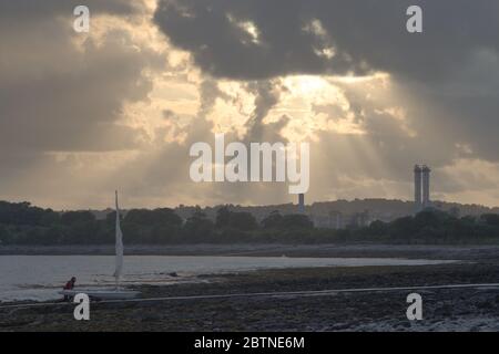 Ein Mann schiebt seine Yacht an einem steinigen Strand auf einen Steg, hinter ihm liegen Fabrikhochhäuser in südwales Stockfoto