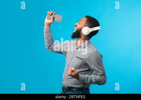 Afro Mann singt mit Smartphone als Mikrofon Stockfoto