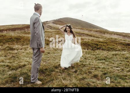 Glücklich wunderschöne Braut läuft zu Bräutigam und Spaß, Luxus-Zeremonie in den Bergen mit herrlichem Blick, Raum für Text, Boho Hochzeitspaar Stockfoto