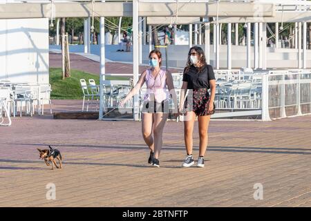 Huelva, Spanien - 23. Mai 2020: Frau, die ihren Hund bei Sonnenuntergang an der Huelva Promenade entlang geht, während des Alarmzustandes eine schützende oder medizinische Gesichtsmaske trägt Stockfoto