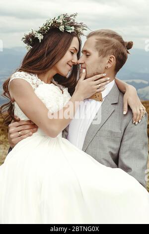 Stilvolle Bräutigam tragen glückliche Braut und umarmen, romantische zärtliche Moment, Boho Hochzeitspaar, Luxus-Zeremonie in den Bergen Stockfoto