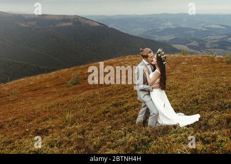 Wunderschöne Braut und stilvollen Bräutigam umarmt, Boho Hochzeit Paar, Luxus-Zeremonie in den Bergen mit herrlichem Blick, Raum für Text Stockfoto