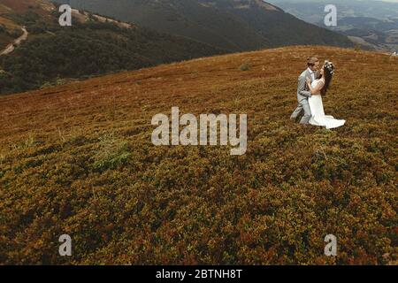 Wunderschöne Braut und stilvollen Bräutigam umarmt, Boho Hochzeit Paar, Luxus-Zeremonie in den Bergen mit herrlichem Blick, Raum für Text Stockfoto