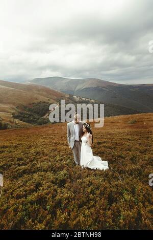Wunderschöne Braut und stilvollen Bräutigam zu Fuß, Boho Hochzeit Paar, Luxus-Zeremonie in den Bergen mit herrlichem Blick, Platz für Text Stockfoto