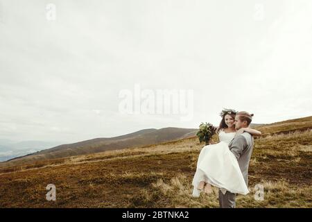 Stilvolle Bräutigam tragen glückliche Braut und Spaß, Boho Hochzeit Paar, Luxus-Zeremonie in den Bergen mit herrlichem Blick, Raum für Text Stockfoto