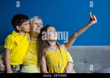 Eine alte Großmutter und ihre geliebten Enkelkinder sitzen zu Hause und fotografieren auf ihrem Smartphone Stockfoto