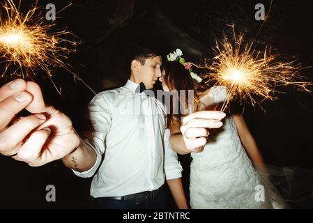 Glücklich schöne Braut und eleganten stilvollen Bräutigam hält Feuerwerk auf der Spitze eines Berges am Abend Stockfoto