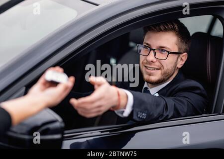 Junger bärtiger Mann, der den Auto-Schlüssel nimmt und auf dem Fahrersitz sitzt Stockfoto