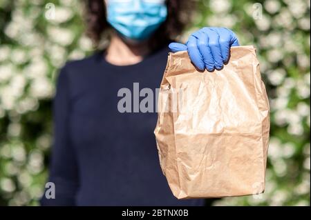 Person in chirurgischen Maske und Schutzhandschuhe liefert online Einkäufe in braunen Papiertüten. Stockfoto