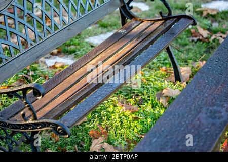 Selektiver, flacher Fokus auf Wassertropfen nach starkem Regen auf einer hölzernen Parkbank mit verschwommenem grünen Hintergrund des Gartenhofs. Diagonale Ansicht. Aufgenommen im Dorf Porto Lagos in Griechenland Stockfoto