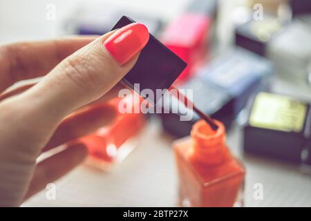 Weibliche Hand halten Pinsel mit rotem Nagellack. Ein Tisch mit einem Haufen Nagellacke in verschiedenen Farben in Unschärfe. Stockfoto