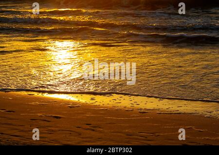 Die Farben des Sonnenuntergangs erscheinen am Ufer des Ostseestands in Kolobrzeg. Sand und Wasser haben die Farbe der goldenen Farben der Abendsonne angenommen Stockfoto