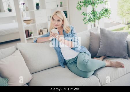 Foto von attraktiven Alter reifen heimelige Hausfrau sitzen bequeme Sofa Couch Kaffee trinken friedlich gute Stimmung entspannend genießen zu Hause Quarantäne bleiben Stockfoto