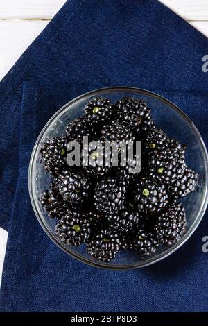 Saftige Brombeerbeeren liegen in einem Glasteller auf einem weißen Holztisch Stockfoto