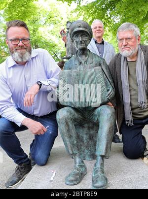 Rostock, Deutschland. Mai 2020. Nach der Enthüllung des Denkmals für den 'Instrel-Großvater' Michael Tryanowski (1919-2018) knien der Oberbürgermeister Claus Ruhe Madsen (l-r) (überparteilich) und der Bildhauer Wolfgang Friedrich neben der Skulptur am Universitätsplatz, im Hintergrund Frank Kraschewski, Sohn. Das Rostocker Original Michael Tryanowski wurde zu seinem 95. Geburtstag am 12.12.2014 mit einem Eintrag in das Ehrenbuch der Hanse- und Universitätsstadt Rostock geehrt. Quelle: Bernd Wüstneck/dpa-Zentralbild/ZB/dpa/Alamy Live News Stockfoto