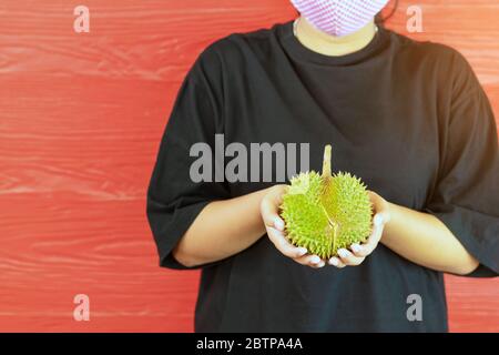 Junge Frau trägt eine Schutzmaske, um eine Infektion des Corona-Virus (Covid-19) in einem schwarzen Hemd mit einem reifen Durian zu verhindern, bereit, mit dem roten w zu essen Stockfoto