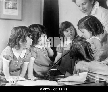 Quint macht einen guten Zuhörer. Foto zeigt: Dionne Quintuplets sprechen mit ihrem eigenen Arzt, Allan Defoe, am Telefon im Kinderzimmer in Callander, Ontario. Dr. Defoe macht einen besonderen Punkt der Anruf die fünf Biesen jeden Tag per Telefon. 13 Juni 1937 Stockfoto