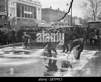 Ealings Anti-Gas-Trupps bei der Arbeit. Von einer interessierten Menge beobachtet und mit dem Verkehr auf der Hauptstraße vorbei, demonstrierten freiwillige Mitglieder der Anti-Luft-Razzia-Truppe von Ealing Councils vor dem Rathaus in Ealing, London, Anti-Gas-Methoden. Das Foto zeigt die Truppe, die in Masken und Sonderanzügen einen Bereich außerhalb des Rathauses von Ealing dekontaminiert, in dem eine 'musterförmige Gasbombe' gefallen ist. Februar 1938 Stockfoto