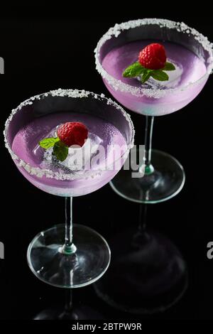 Cocktailgläser mit rosa Gin und Tonic garniert mit großem Stück Eis, Pfefferminze und Himbeere mit Salzkristallen am Glasrand Stockfoto