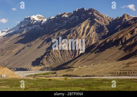 Steile, hohe, schroffe Berge, die über dem Spiti Fluss und den grünen Feldern in der Stadt Kaza in Himachal Pradesh, Indien, emporragen. Stockfoto