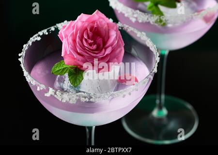 Zwei hohe Cocktailgläser mit rosa Gin und Tonic garniert mit großen Salzkristallen auf einem Rand eines Glases, großes Stück Eis, Pfefferminze Stockfoto