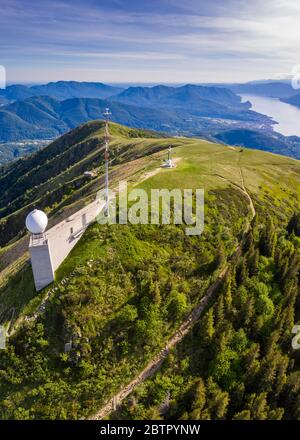 Luftaufnahme vom Gipfel des Monte Lema in Richtung Lago Maggiore mit seiner Seilbahn und Hütte. Lugano Prealps, Kanton Tessin, Schweiz. Stockfoto