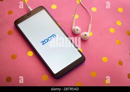 Zoom mobile Anwendung auf einem Smartphone mit Kopfhörern auf einem rosa Kissen. Zoom-Benutzer können Sitzungen aufzeichnen und an Projekten zusammenarbeiten. Stockfoto