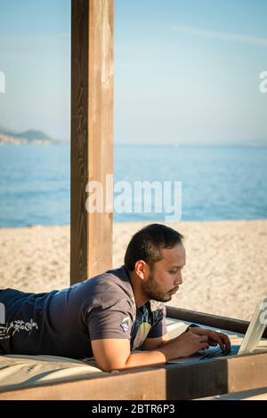 Ein Mann, der einen Laptop im Freien am Strand benutzt Stockfoto