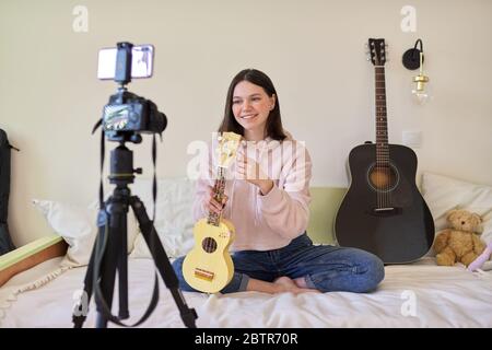 Teenager-Mädchen spielt Musik auf Ukulele, Online-Lernen und Chat mit Anhängern Stockfoto